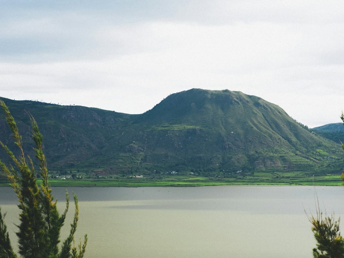 Mountain with green, cultivated slopes above the calm waters of Lake Itasy at Ampefy, framed by conifers.