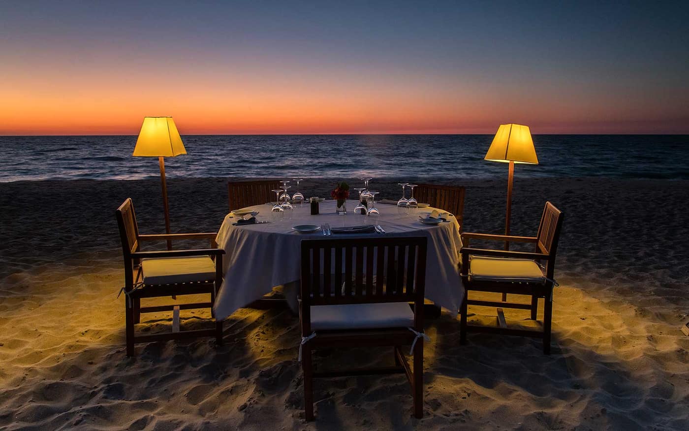 Table set on the beach at sunset, lit by two lamps