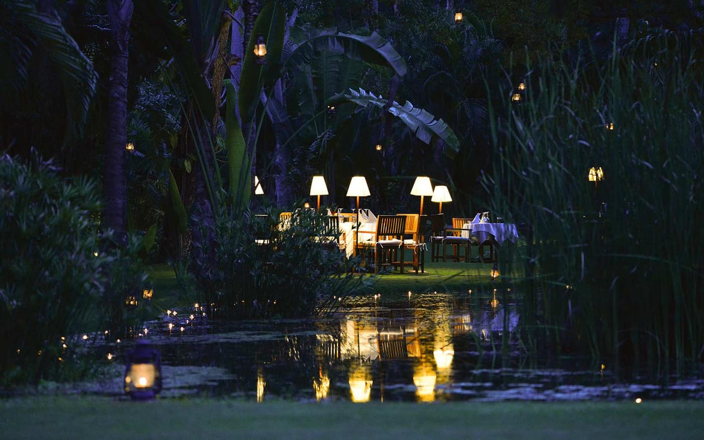 Tables set and lit at nightfall, beside a pond in the garden