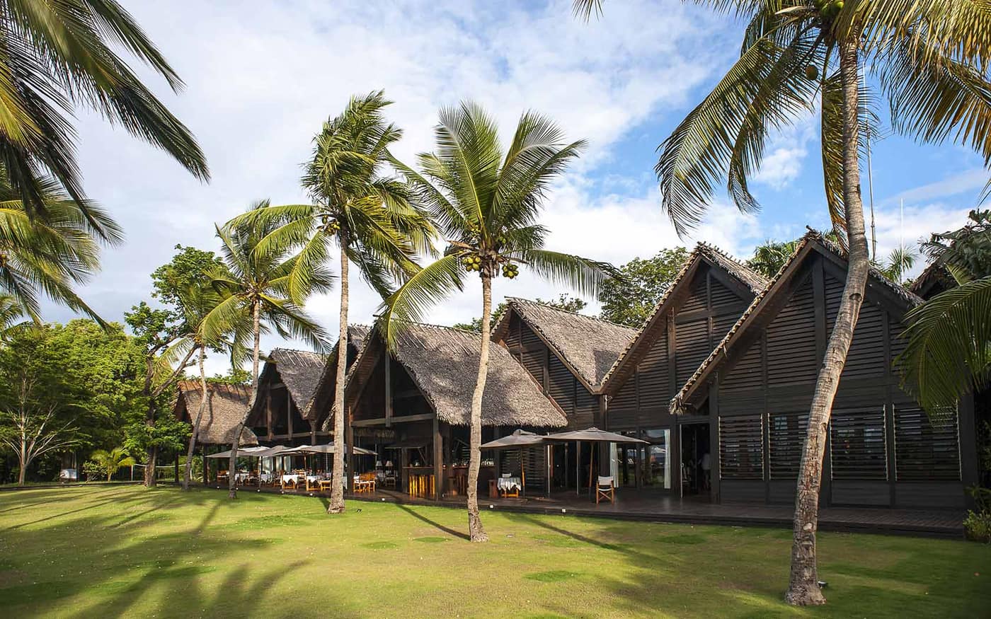 The lodge's thatched roofs, among palm trees and lawn