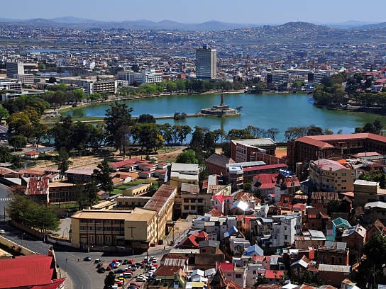 High view over the rooftops and buildings of Antananarivo, with Lake Anosy and hills in the background.