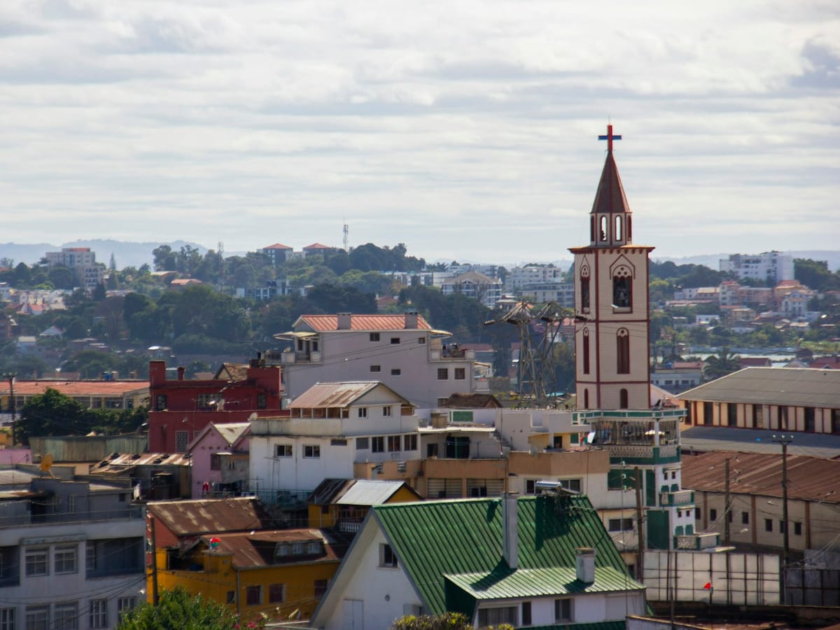 Church bell tower topped with a cross rising above the rooftops and colourful houses of an Antananarivo district.