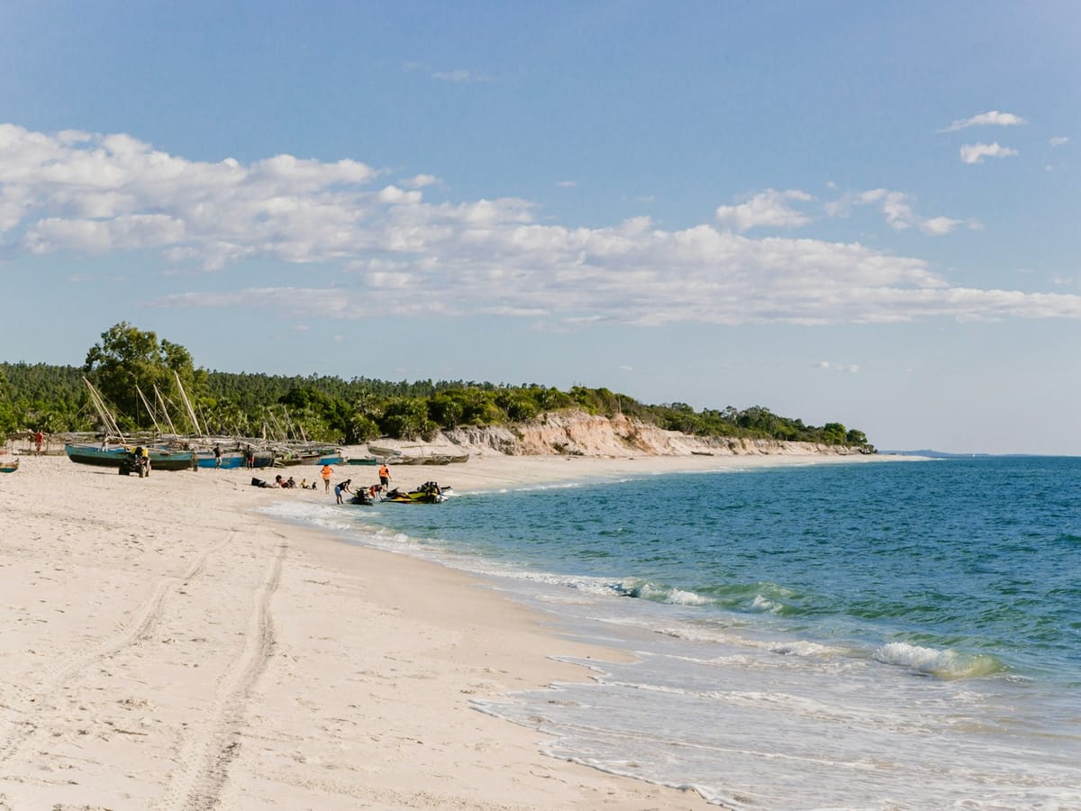 White sandy beach at Antsanitia backed by forest and pale cliffs, with pirogues and a few people by the water.