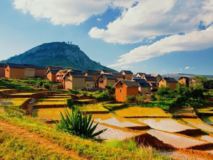 Hamlet of brick houses above terraced rice fields at the foot of a rocky hill, in the Vakinankaratra highlands.
