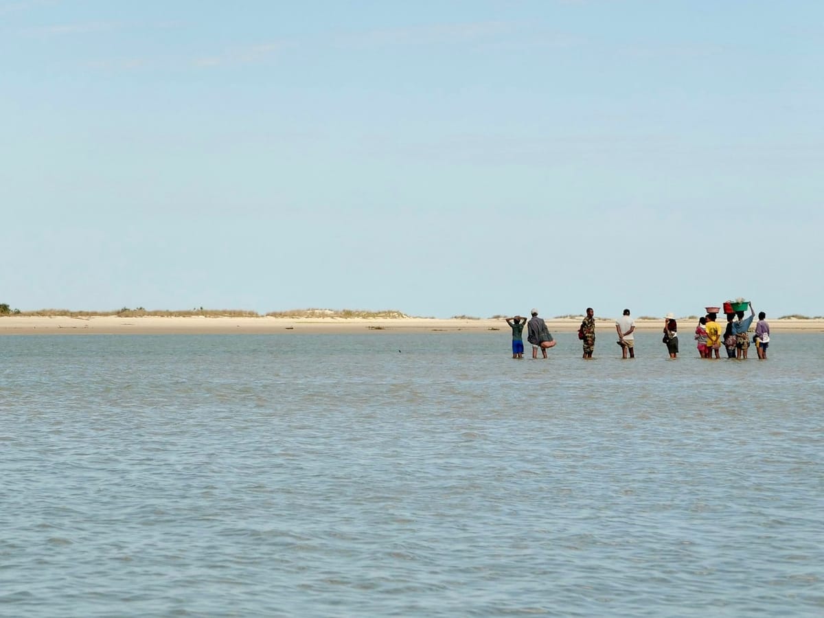 Local people wade across a shallow lagoon towards a sandy shore near Morondava, some carrying basins on their heads.