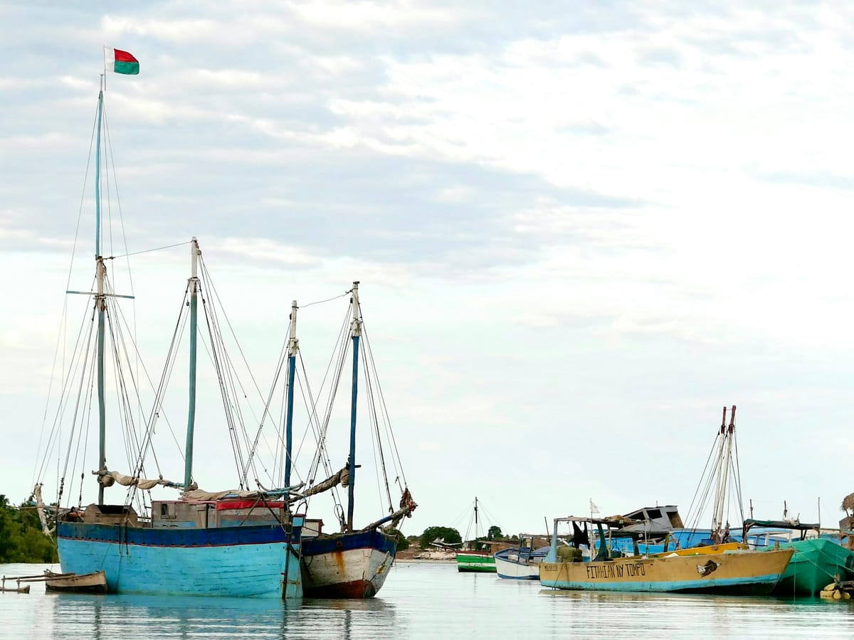 Two-masted wooden dhows at anchor, the Malagasy flag at the masthead, beside brightly painted fishing boats.