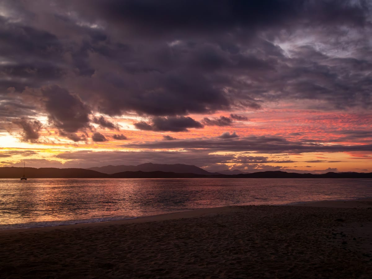 Purple and pink clouds above the sea and a beach at sunrise on Nosy Iranja.