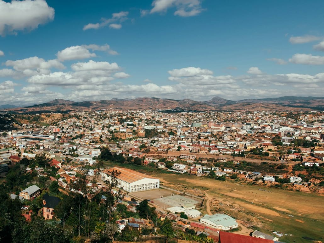 High view over Fianarantsoa, its houses and rooftops stretching towards the hills beneath a sky dotted with clouds.