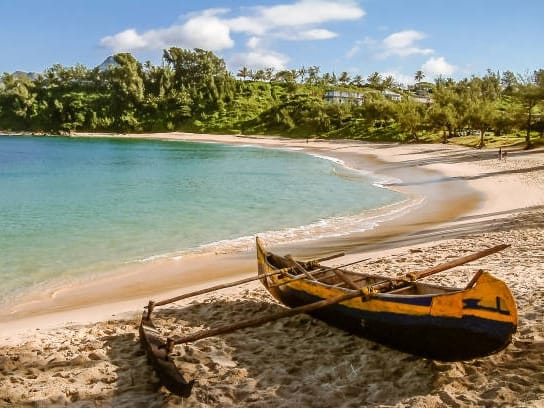 Yellow and blue outrigger canoe on the sand of a small turquoise bay in Fort Dauphin.