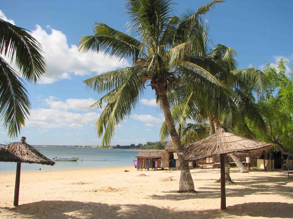 Sandy beach at Ifaty with coconut palms, thatched parasols and a stall of colourful fabrics by the water.