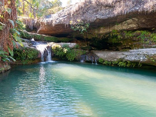 The Natural Pool in Isalo: a small waterfall dropping into a turquoise basin beneath a sandstone overhang and greenery.