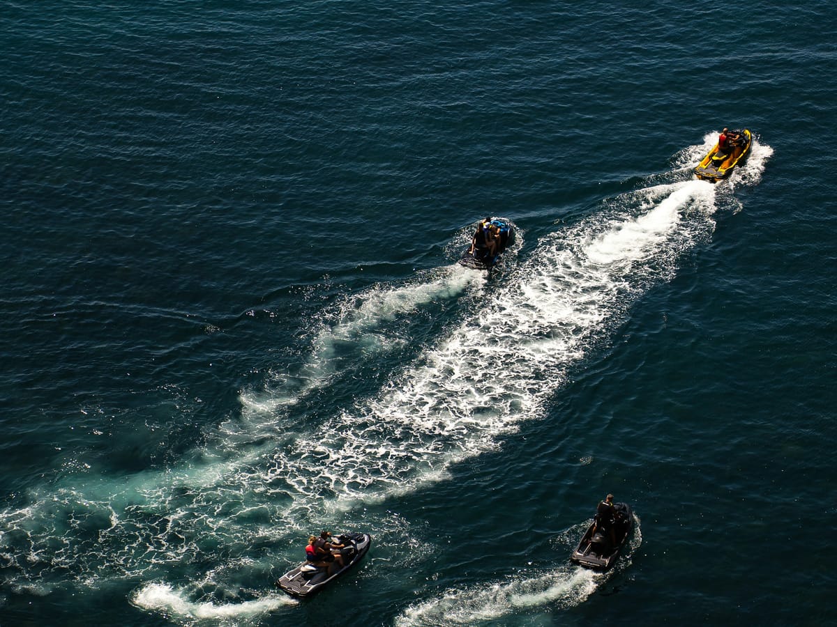 Four jet skis seen from above, leaving long white wakes across a dark sea.