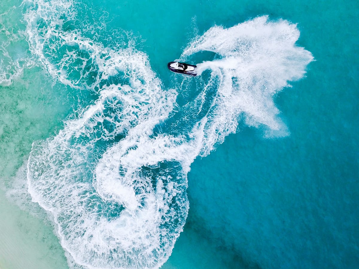 A jet ski seen from the air, drawing wide loops of white foam on turquoise water.