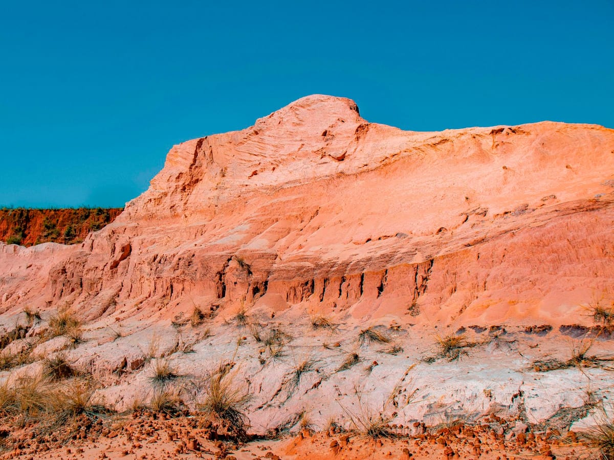 Pink and white rock face carved by erosion and dotted with dry grass tufts at the Cirque Rouge, Mahajanga.