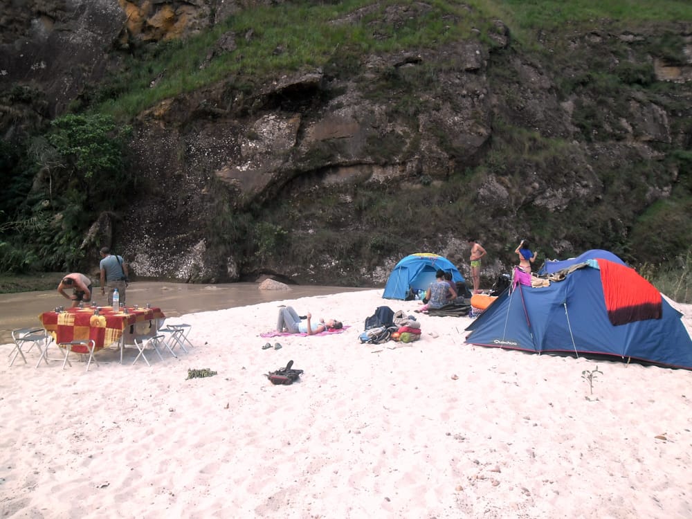 Camp with tents and a laid table on a white sandbank at the foot of a cliff in the Makay.