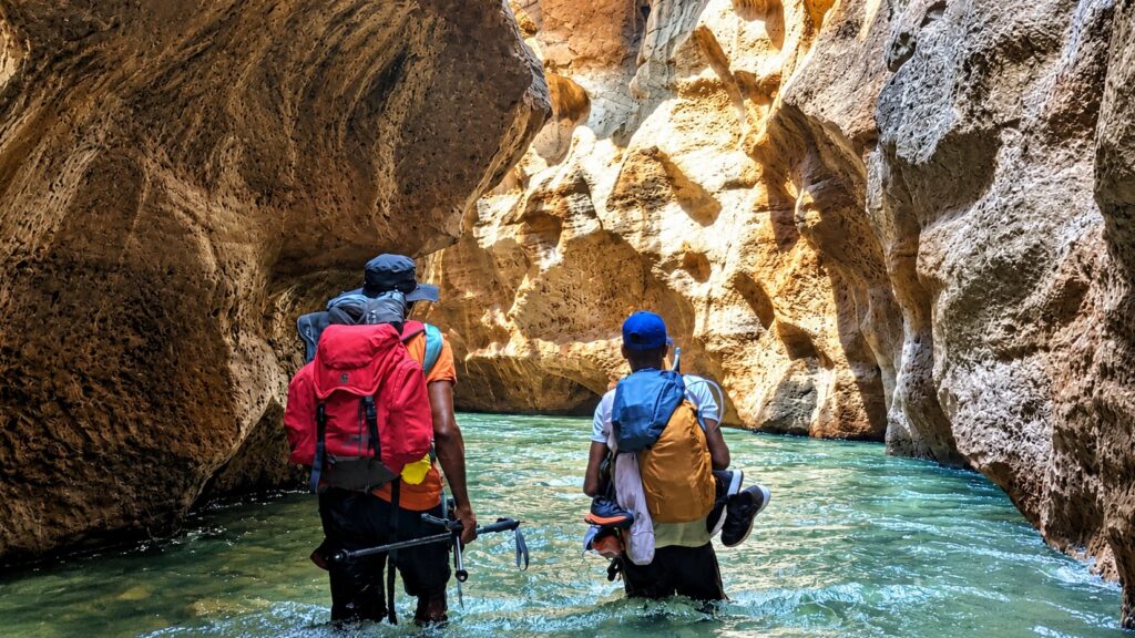 Hikers wading up the turquoise river of a Makay canyon, between towering sandstone walls