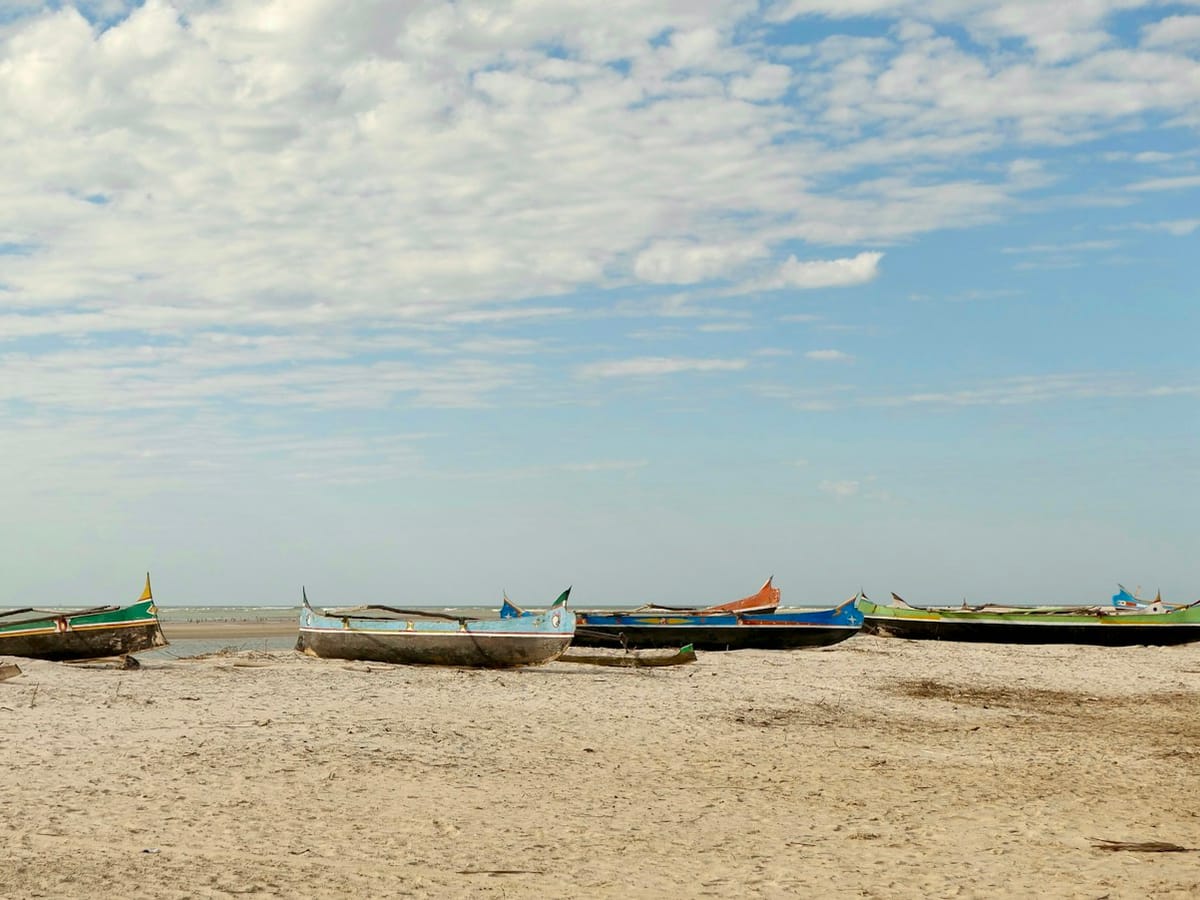 Colourful dugout canoes pulled up on a wide sandy beach at Morondava beneath a lightly clouded sky.