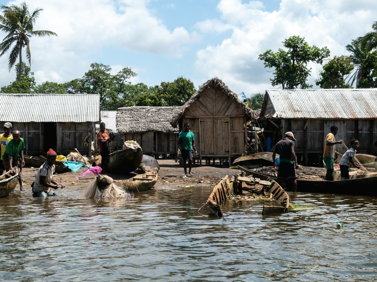 Fishermen rinsing a net in the water in front of a village of wooden and tin-roofed houses, among dugout pirogues, in Madagascar.