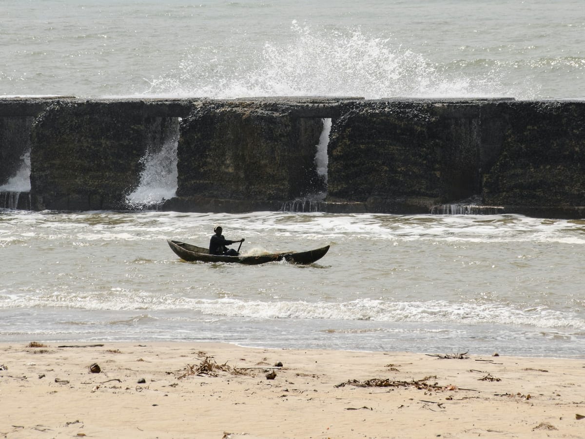A fisherman paddling a dugout canoe in front of a sea wall lashed by waves on the Manakara shoreline.