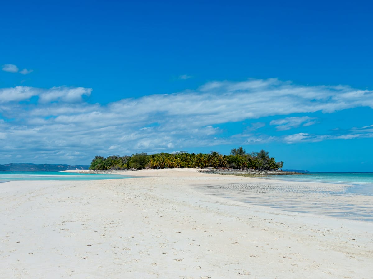 A long white sand beach facing a wooded islet across the turquoise sea at Nosy Iranja.
