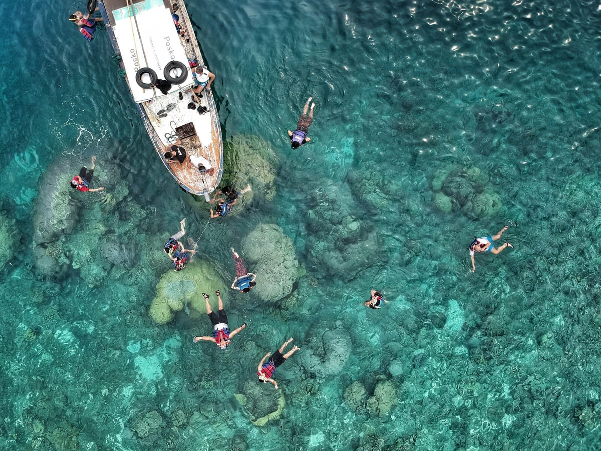 Aerial view of snorkellers around a boat anchored above coral heads in turquoise water.