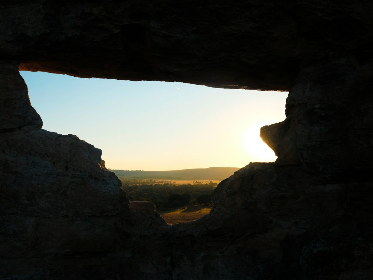 The low sun on the horizon seen through a natural opening in the rock, looking out over a wooded plain, in Madagascar.