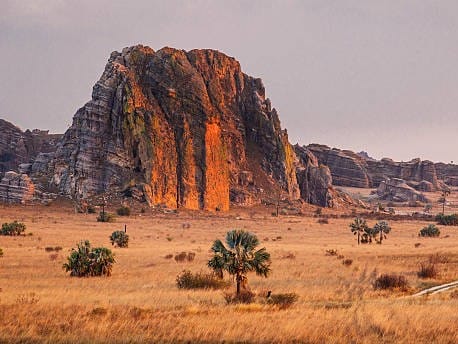 Sandstone massif with orange cliffs rising above a savannah of dry grass and palms, on the outskirts of Ranohira.