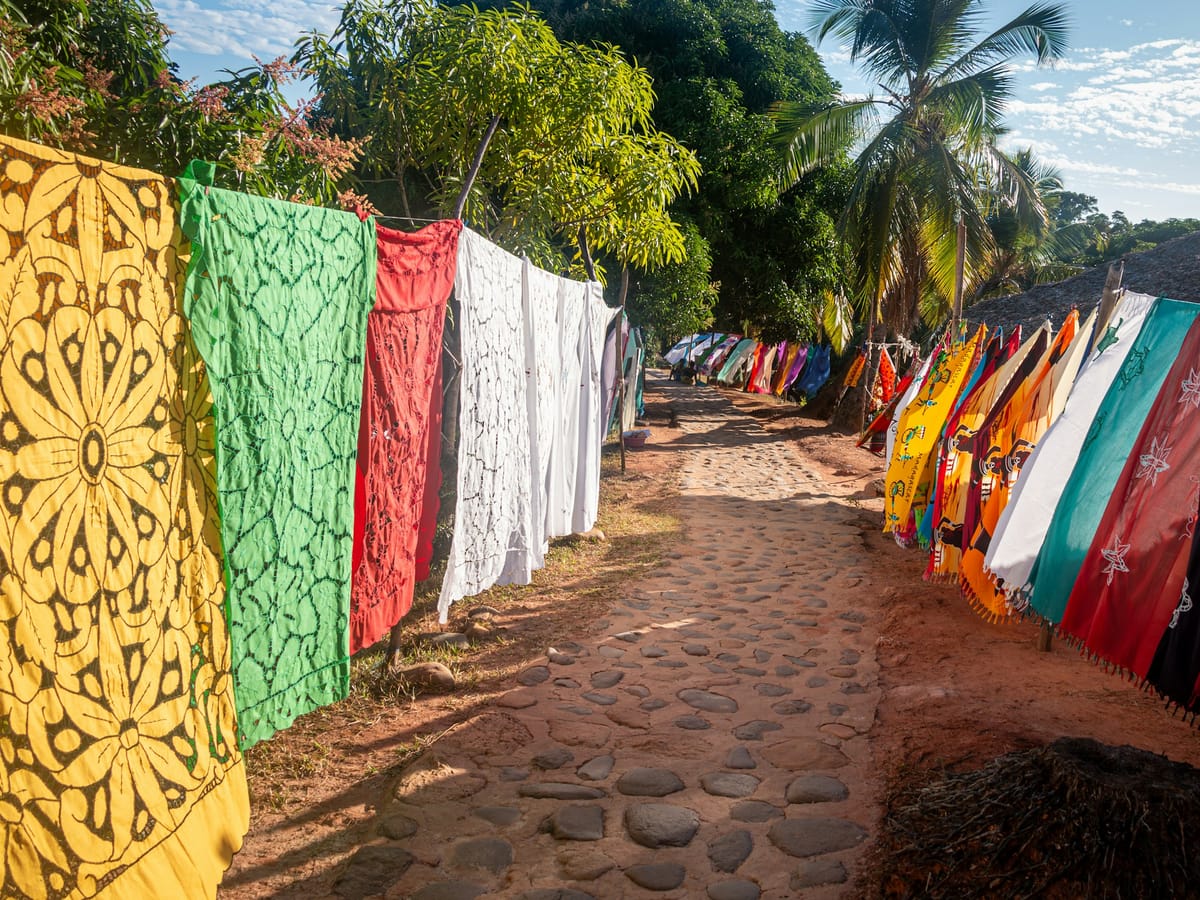 Openwork tablecloths and colourful sarongs hung on both sides of a cobbled path beneath the palms, on the island of Nosy Iranja.