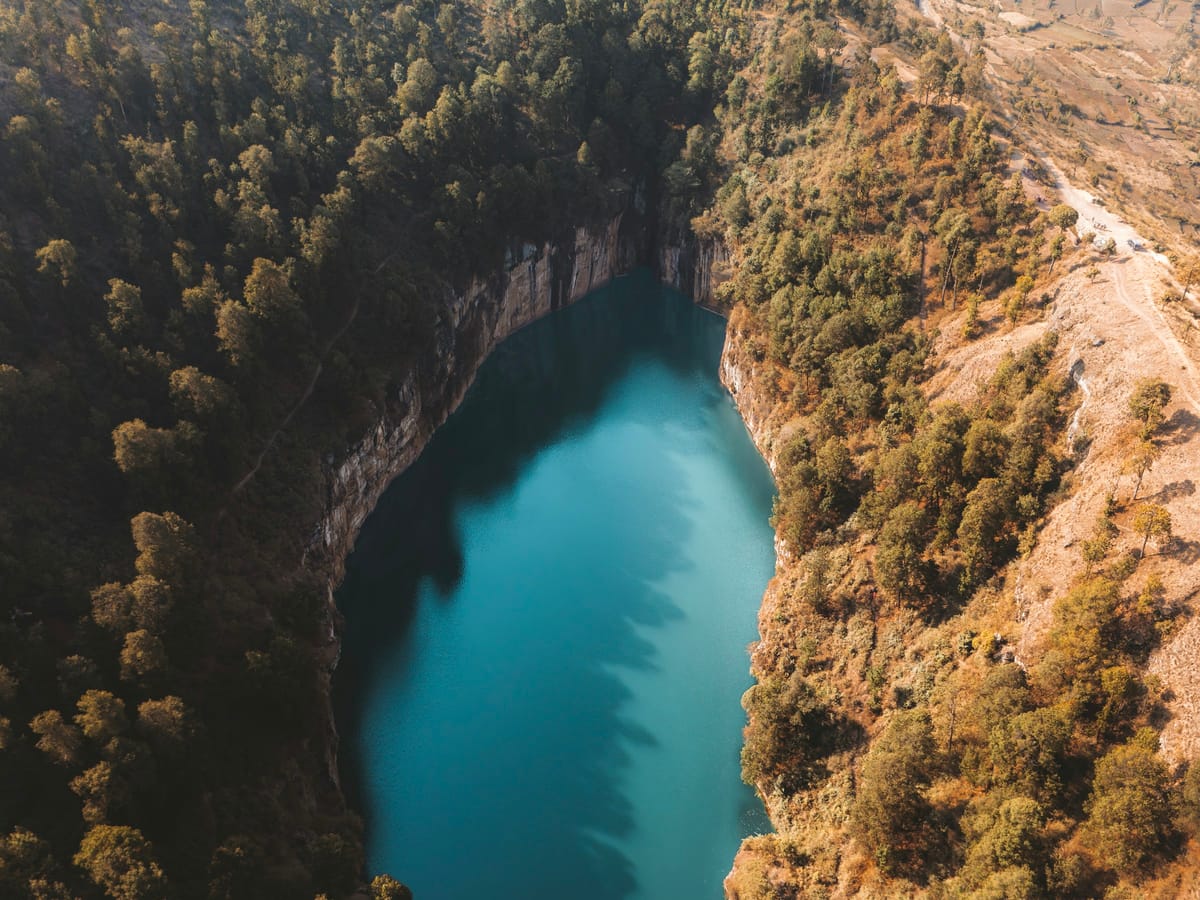 Aerial view of a turquoise crater lake hemmed in by cliffs and forest in the Antsirabe area.