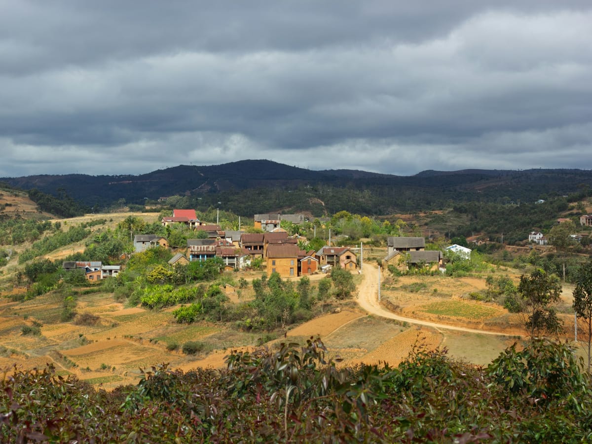 A village of brick houses surrounded by hills and fields in Madagascar, beneath a heavy sky.