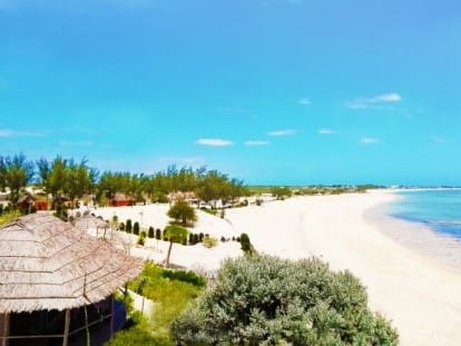 Long white-sand beach at Salary, lined with casuarina trees and bungalows, facing a turquoise sea.