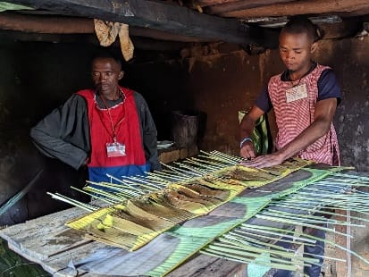 Two craftsmen arranging thin stems and plant strips on a workbench in a workshop at Talata Volonondry.