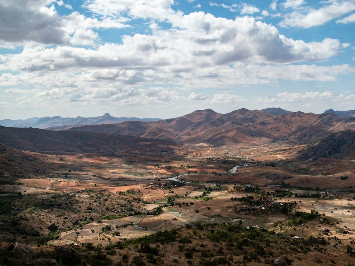 The Tsaranoro Valley seen from above, with dry hills, scattered trees and mountains beneath a cloudy sky.