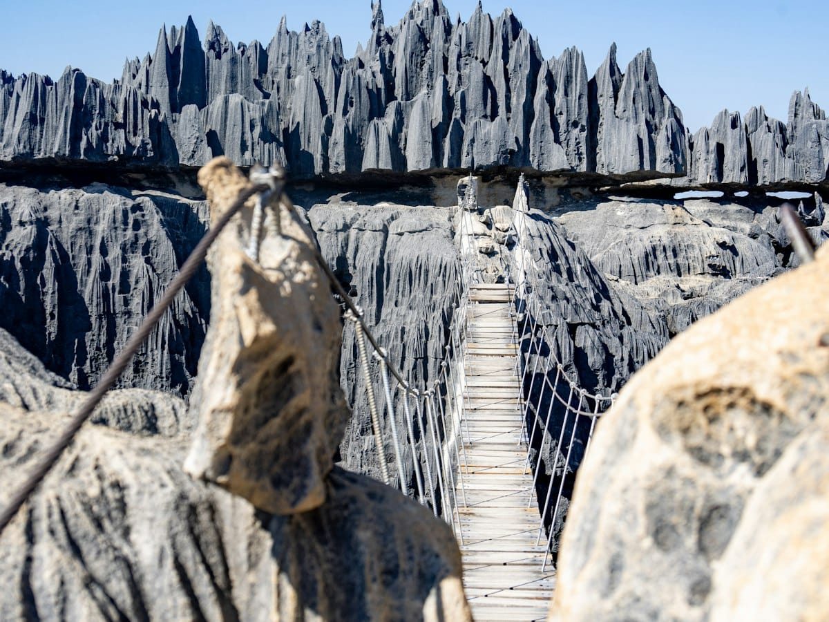 Wooden suspension bridge stretched between the grey limestone pinnacles of the Tsingy de Bemaraha under a blue sky.