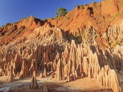 Red earth cliff and a field of pointed pinnacles in sunlight beneath a blue sky at the Red Tsingy.