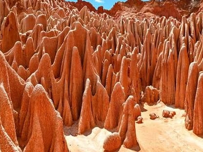 Sandy passage between tall, closely packed orange earth pinnacles at the Red Tsingy, under a patch of blue sky.