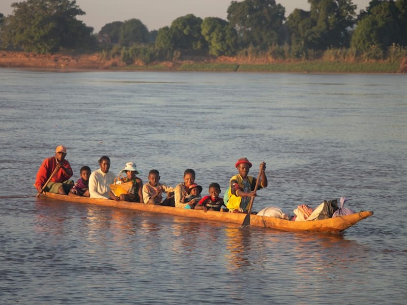 Villagers seated in a long wooden dugout canoe travelling on the calm waters of the Tsiribihina in golden light.
