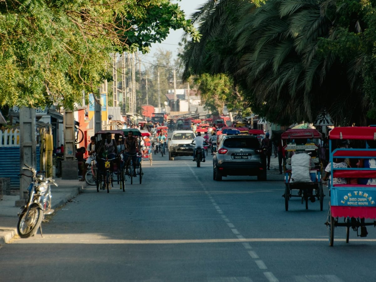 Street in Toliara lined with trees and palms, busy with colourful cycle rickshaws, cars and motorbikes.