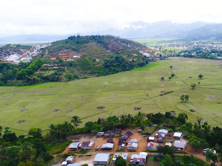 Aerial view of a valley of rice paddies, a village with tin roofs and cloud-capped hills in Madagascar.