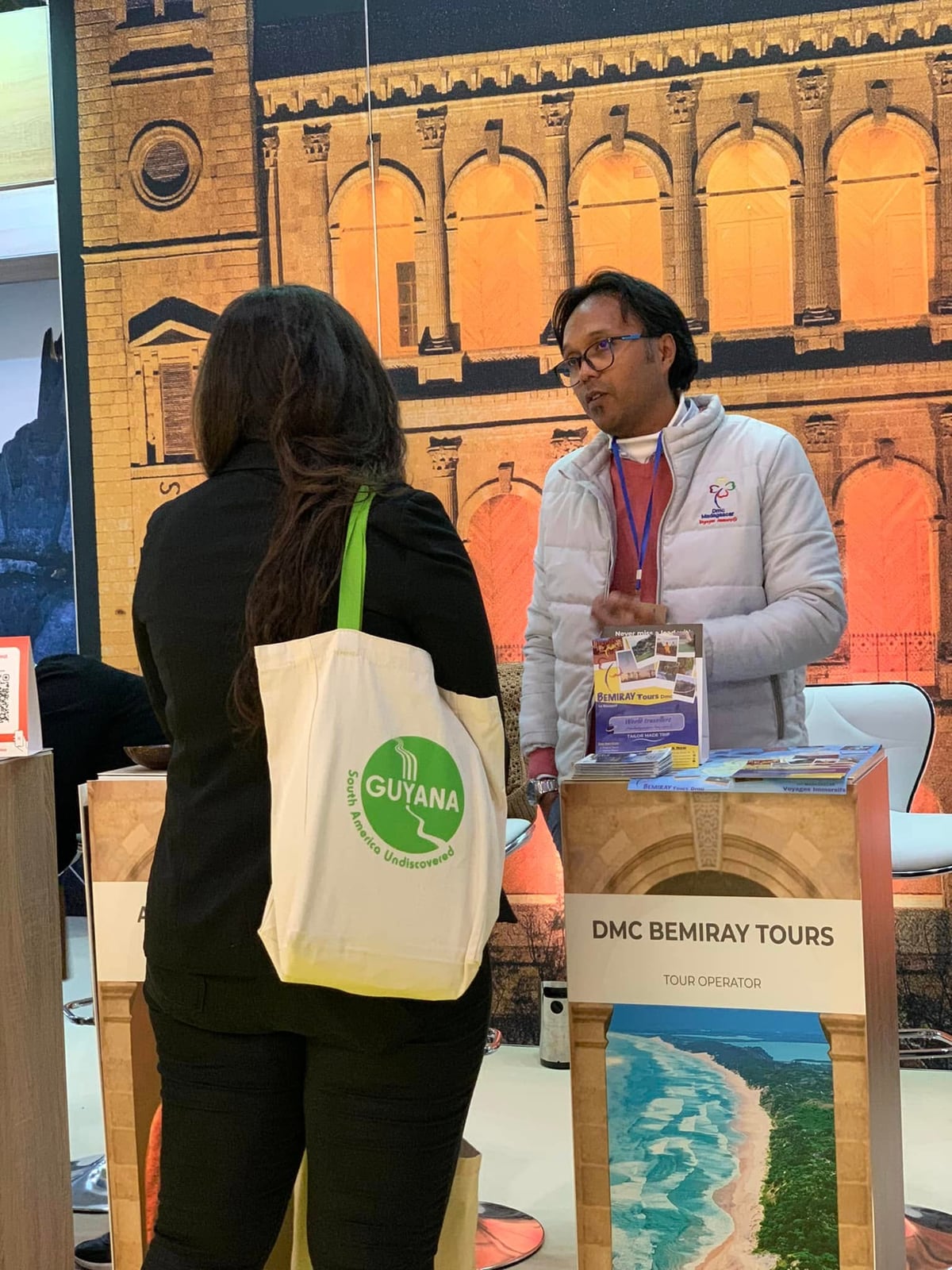 Chatting with a visitor at the DMC Bemiray Tours counter on the stand